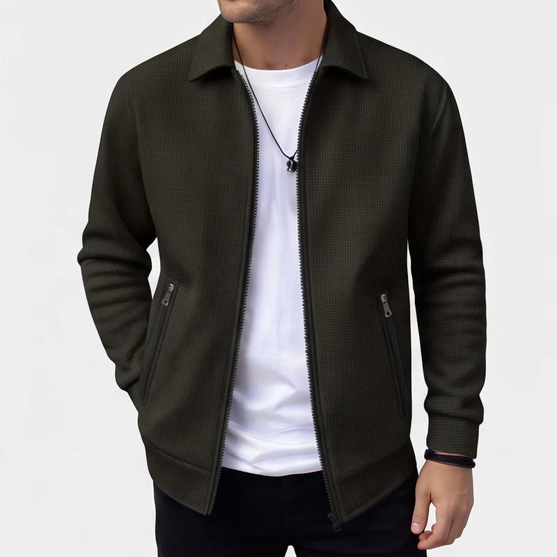 Man wearing an open dark olive knit zip-up jacket with a textured pattern and two zippered pockets.