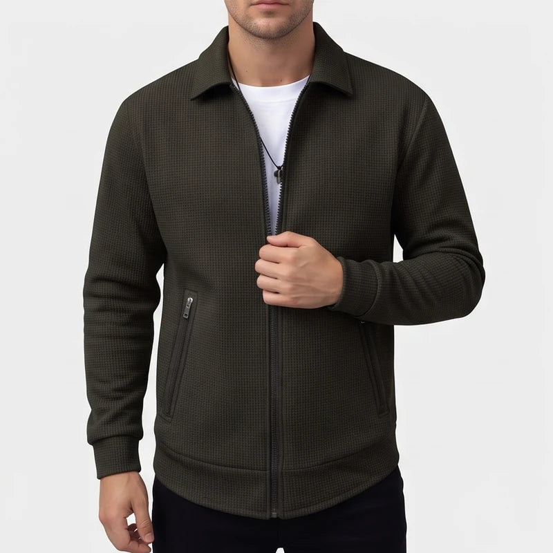 Man wearing a dark green textured knit jacket, partially unzipped, with a collared neck and zippered chest pocket.
