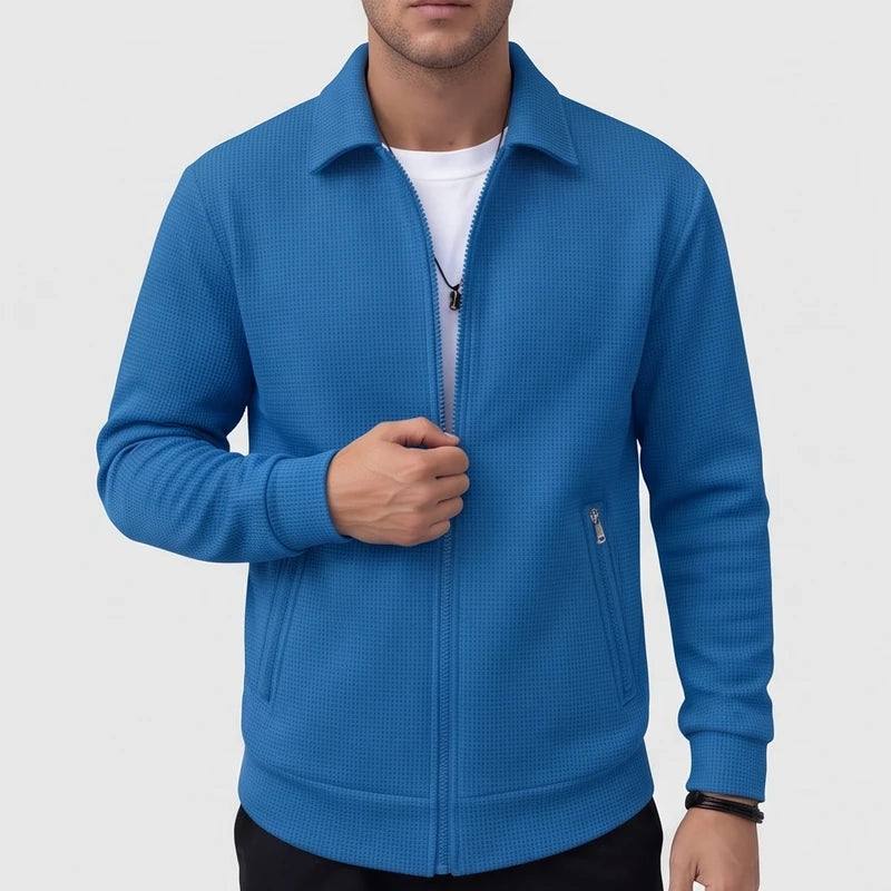 Man wearing a vibrant blue waffle-knit jacket with a collar, partially unzipped over a white t-shirt.