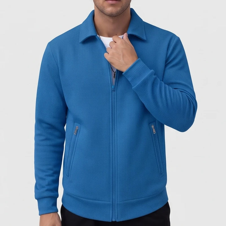 Man wearing a bright blue textured knit zip-up jacket with collar, silver zippers, and ribbed cuffs.
