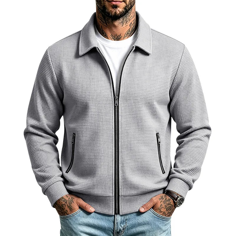 Man wearing a light gray waffle knit zip-up jacket with black zippers, collared neckline, and ribbed cuffs.