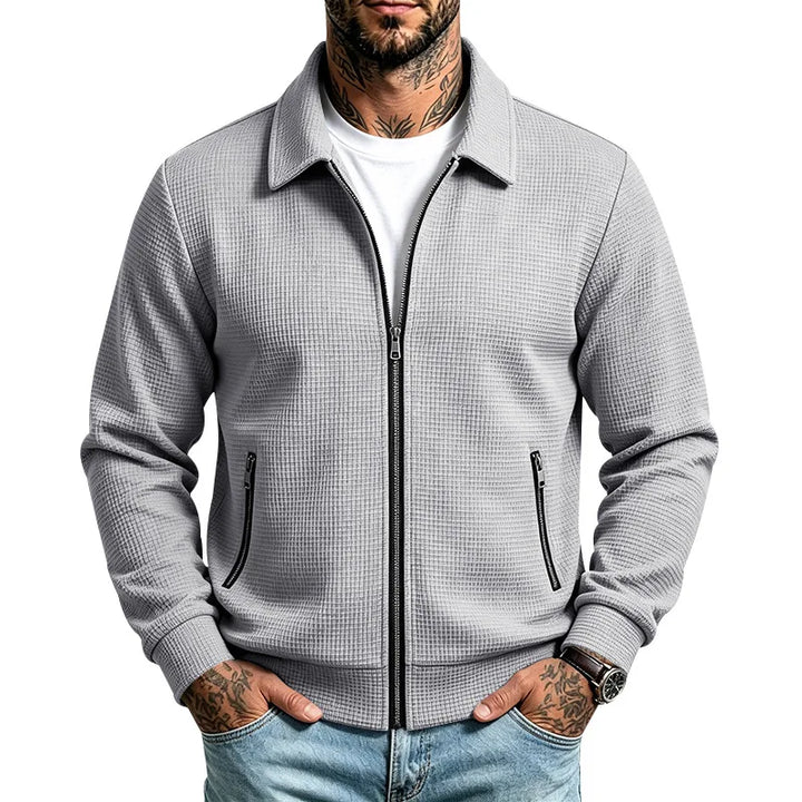 Man wearing a light gray waffle knit zip-up jacket with black zippers, collared neckline, and ribbed cuffs.