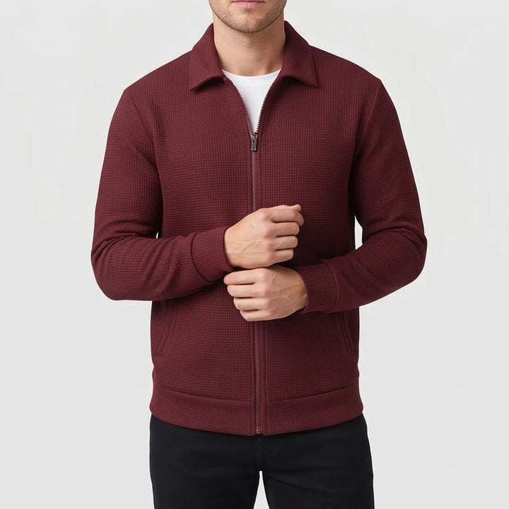 Man wearing a dark red waffle-knit zip-up jacket with a collar and pockets, adjusting his cuff.
