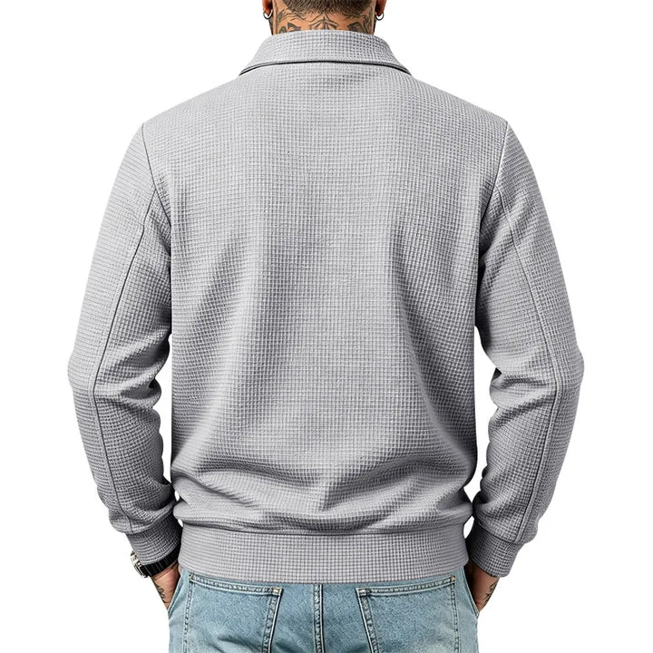 Man wearing a light gray waffle knit jacket with a collar and ribbed hem, paired with blue jeans, seen from the back.