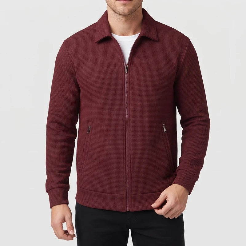 Man wearing a burgundy waffle-knit zip-up jacket with a collar, two zippered pockets, and a white t-shirt underneath.