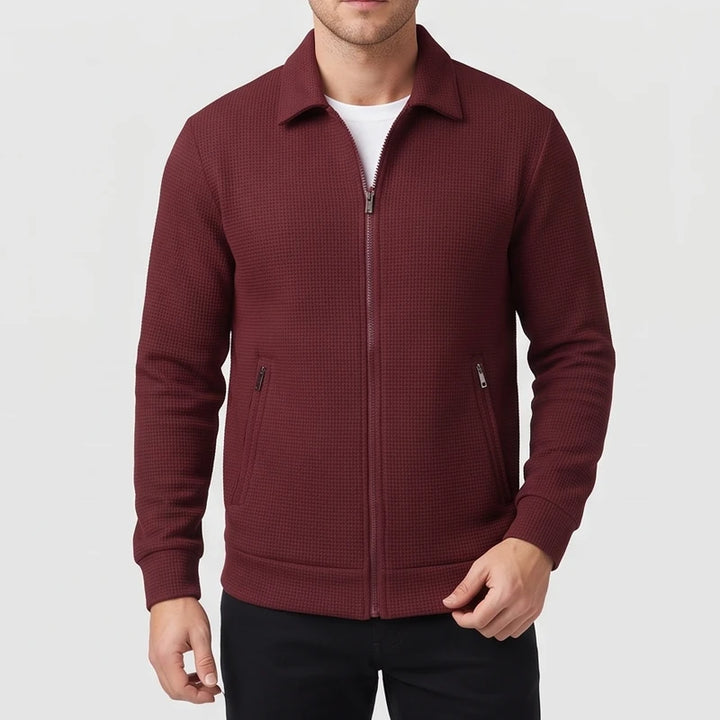 Man wearing a burgundy waffle-knit zip-up jacket with a collar, two zippered pockets, and a white t-shirt underneath.