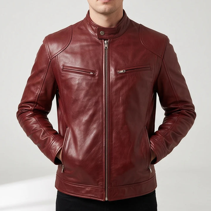 Man wearing a burgundy leather biker jacket with zip pockets, standing with hands in pockets against a plain light background.
