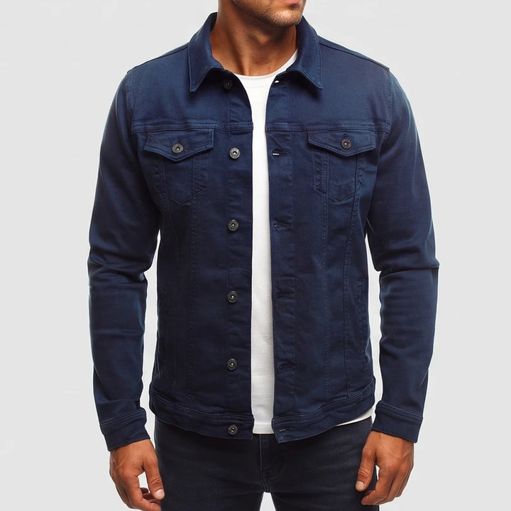 Man wearing a dark blue long sleeve denim jacket with two chest pockets, silver buttons, and a collared neckline.