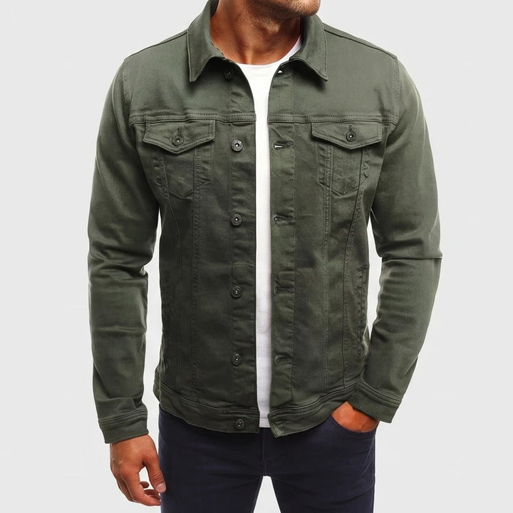 Man wearing an olive green denim jacket with buttoned chest pockets and dark buttons over a white t-shirt.