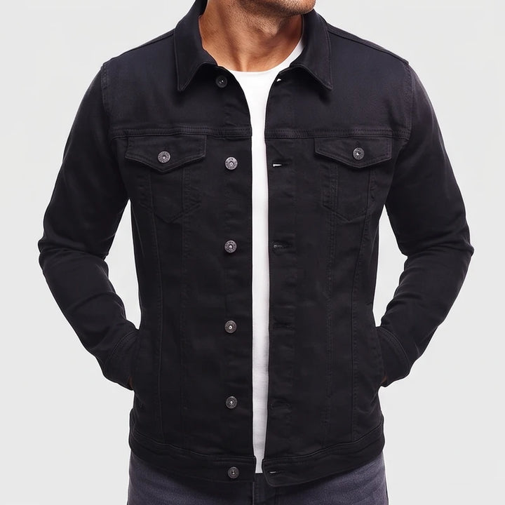 Man wearing a black long-sleeve denim jacket with silver buttons, chest pockets, and hands in hip pockets, over a white tee.
