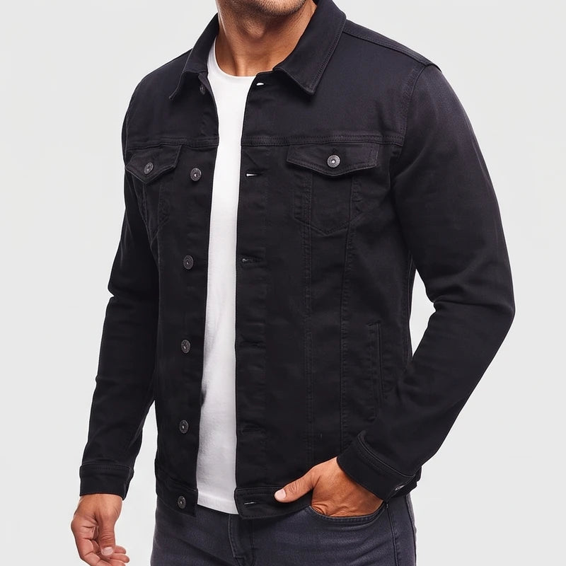 Man wearing a black denim jacket with two chest pockets and metal buttons, his hand in a dark pant pocket.