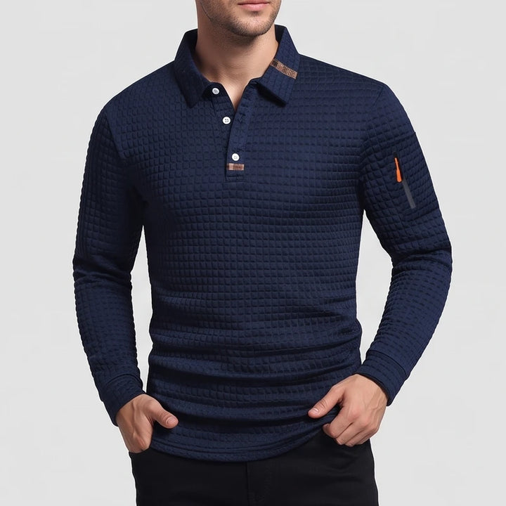 Man wearing a navy blue waffle-knit long sleeve polo shirt with white buttons and a zipper pocket on the left arm.
