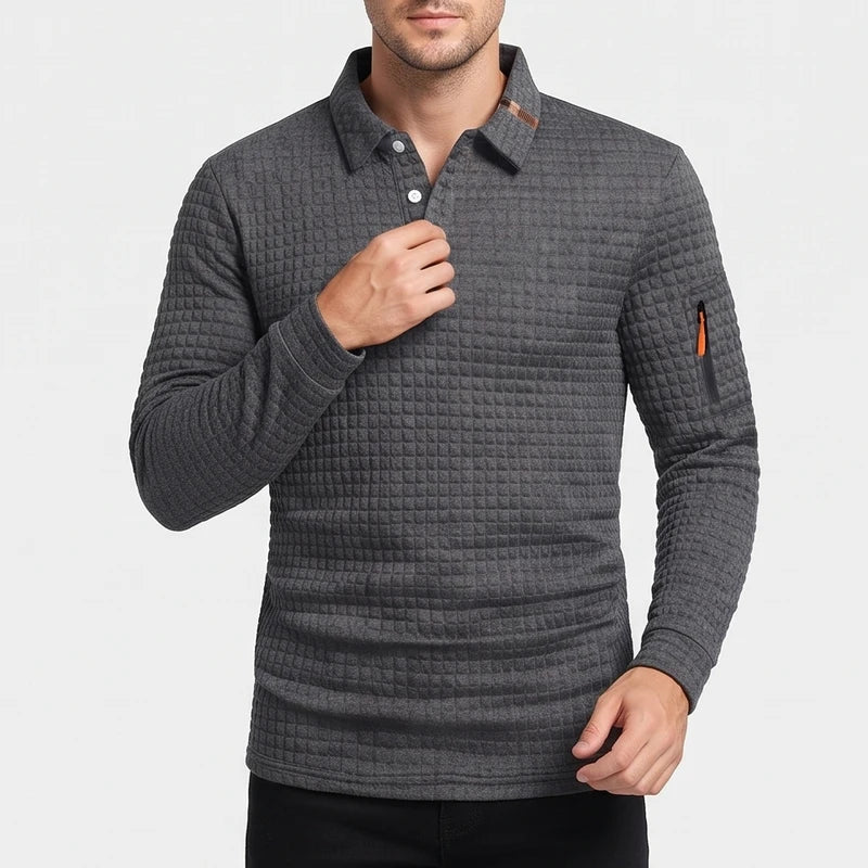 Man wearing a dark gray long-sleeve polo shirt with a quilted texture, white buttons, and an orange zippered arm pocket.