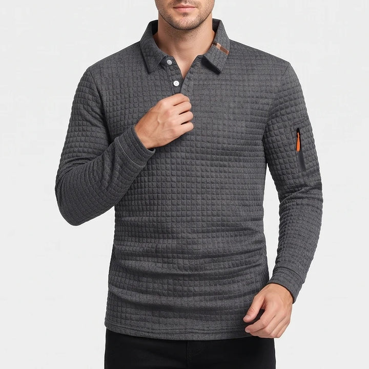 Man wearing a dark gray long-sleeve polo shirt with a quilted texture, white buttons, and an orange zippered arm pocket.