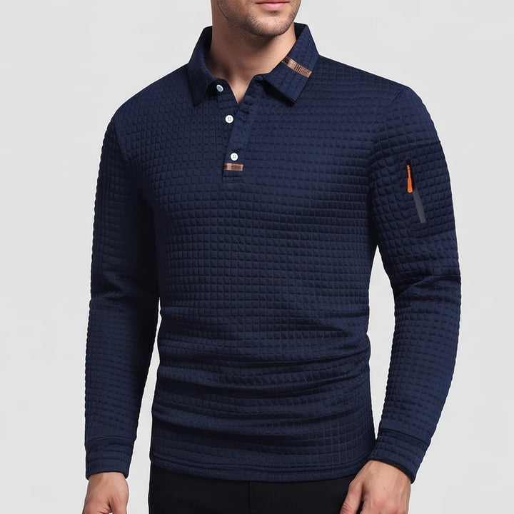 Man wearing a navy blue long-sleeve polo shirt with a quilted texture, white buttons, and an orange sleeve zipper.