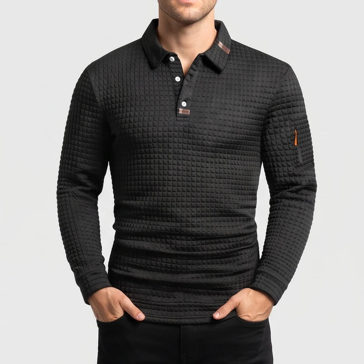 Man wearing a black long-sleeve polo with a quilted texture, white buttons, and a small orange zipper on the left sleeve.
