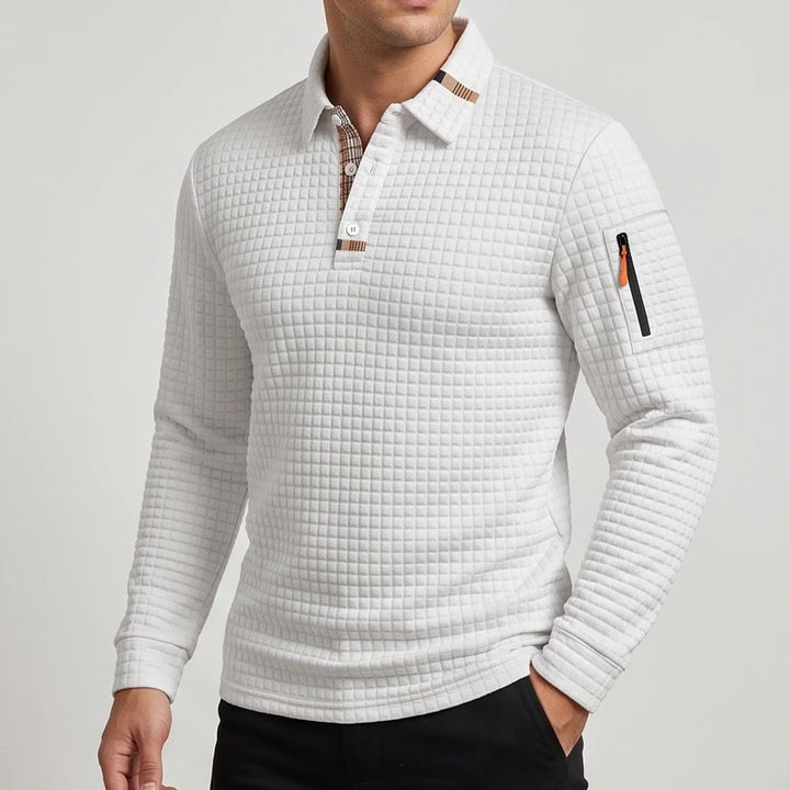 Man wearing a light gray long sleeve quilted polo with a plaid collar lining and an orange zipper on the left sleeve pocket.