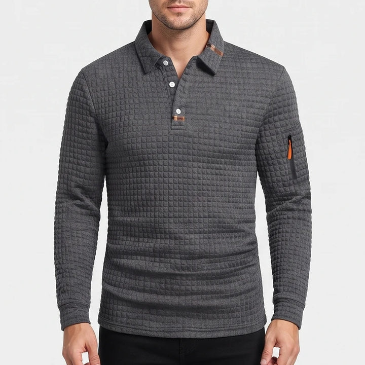 Man wearing a dark gray waffle-knit long-sleeve polo with a three-button placket, contrasting brown collar lining, and orange sleeve zipper.