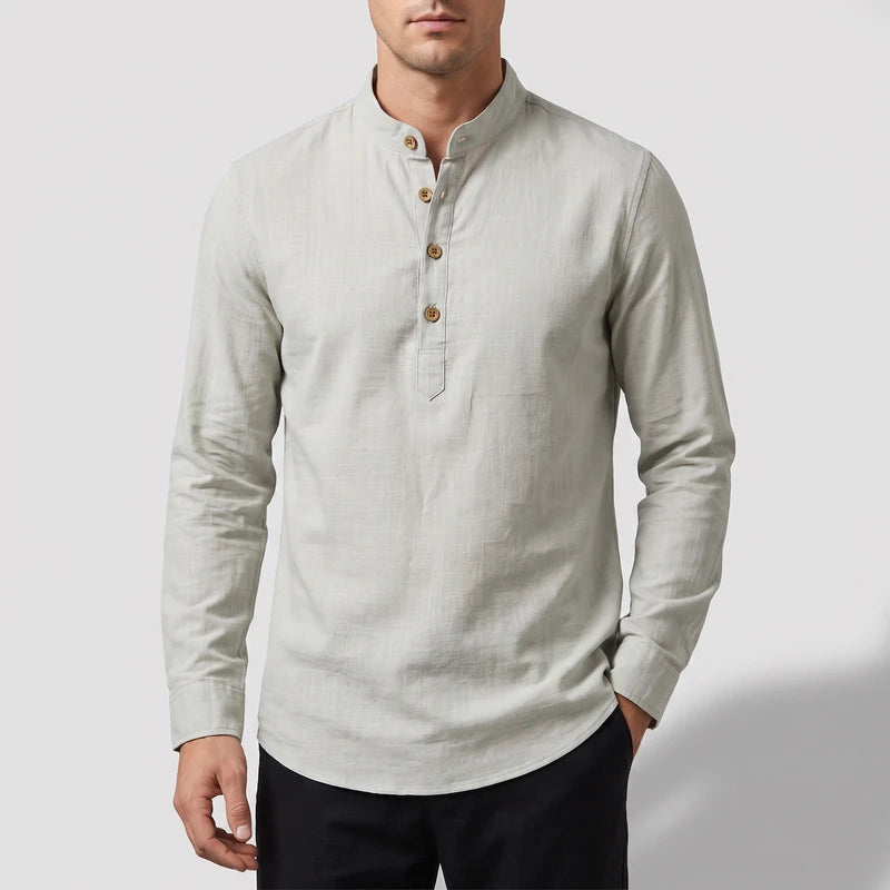 Man wearing a light gray long-sleeve mandarin collar shirt with three wooden buttons and a curved hem, against a light background.
