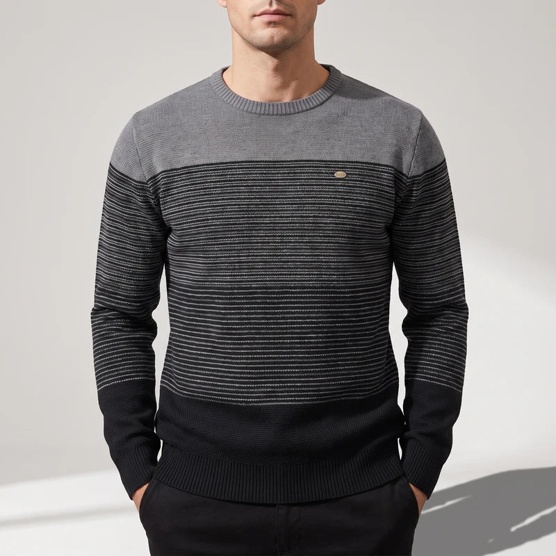 Man wearing a grey and black striped long-sleeve sweater with a contrasting solid grey crew neck on a plain background.