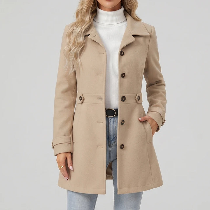 Woman wearing a tan long wool coat with large lapels, dark brown buttons, and front pockets, posed against a white background.