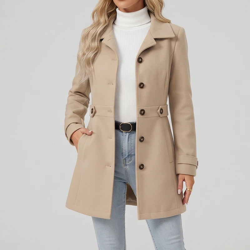 Woman wearing a tan long wool coat over a white turtleneck and light wash jeans, with one hand in her pocket.