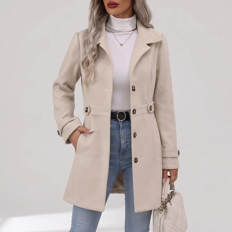 Woman wearing a cream long coat with notched lapels and brown buttons, her hand in a side pocket.