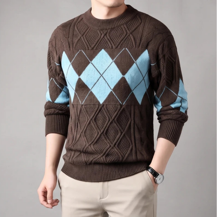 Man wearing a brown argyle knit sweater with light blue diamonds, beige pants, and a dark watch.