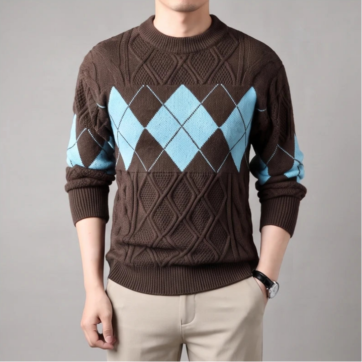 Man wearing a brown knit sweater with a light blue argyle pattern across the chest and sleeves, against a gray background.