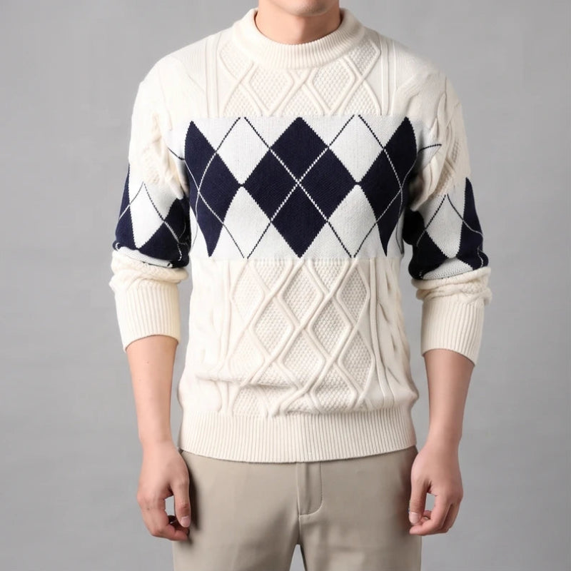 Man wearing a cream knit sweater with an argyle pattern of navy and white diamonds across the chest and sleeves.