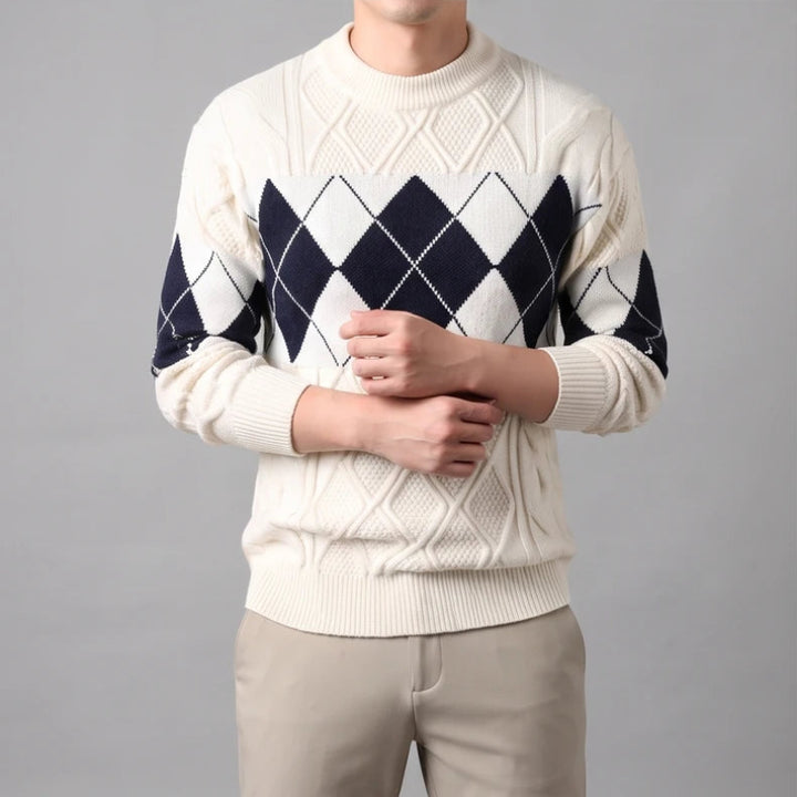 Man wearing a cream cable knit sweater with a navy and white argyle pattern across the chest and sleeves.