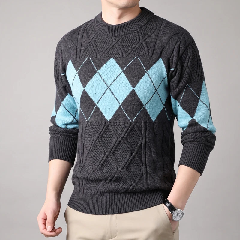 Man wearing a dark gray knit sweater with light blue argyle diamonds on the chest and sleeves, against a plain gray background.