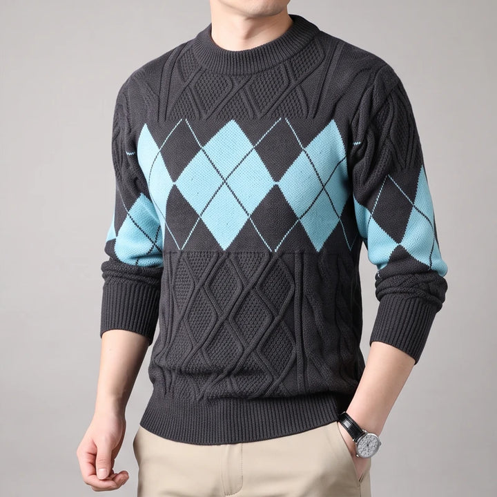 Man wearing a dark gray knit sweater with light blue argyle diamonds on the chest and sleeves, against a plain gray background.