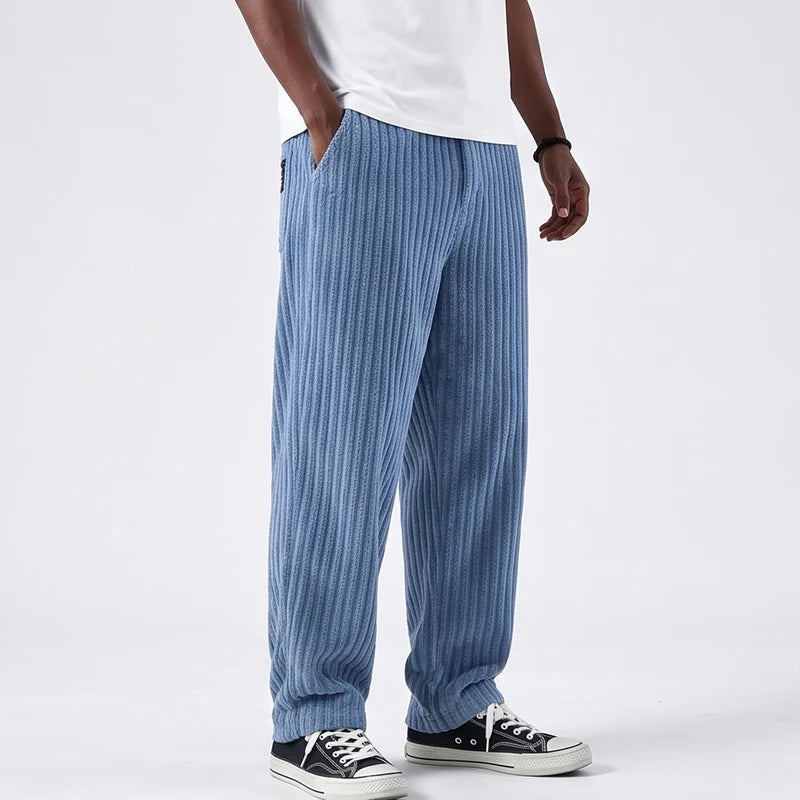 Man wearing light blue corduroy baggy pants with a ribbed texture, one hand in the pocket, paired with black sneakers.