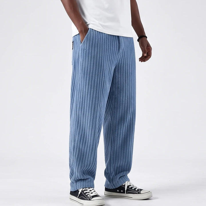 Man wearing light blue corduroy baggy pants with a ribbed texture, one hand in the pocket, paired with black sneakers.