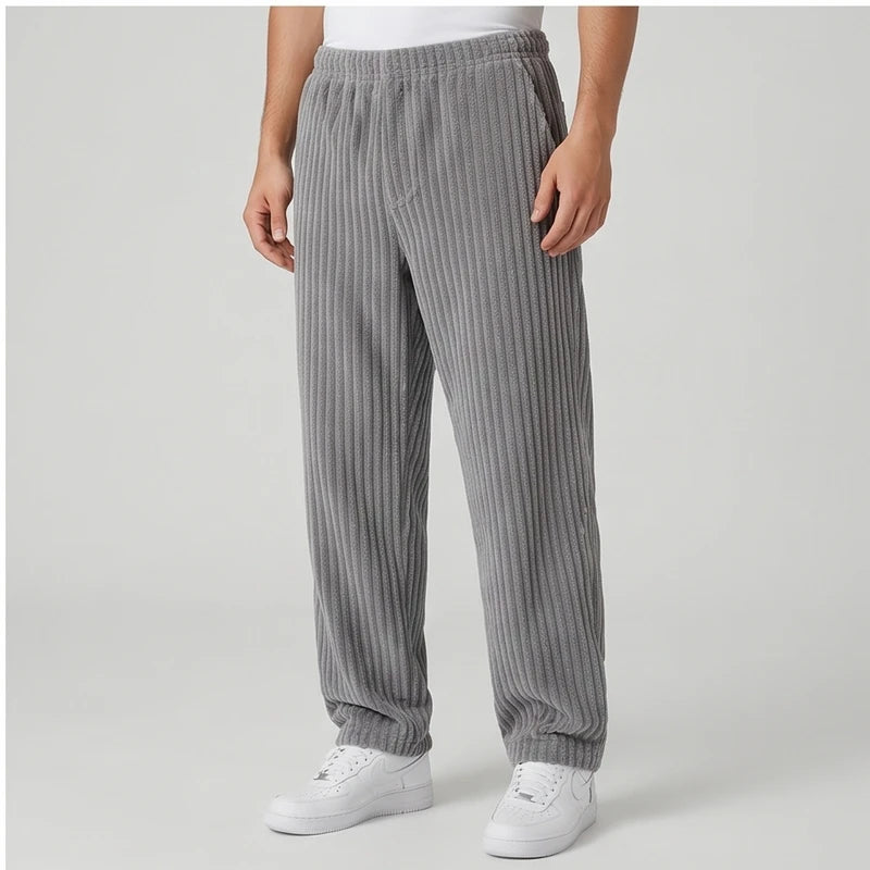 Man wearing baggy gray corduroy sweatpants with an elastic waistband, paired with white sneakers on a light background.
