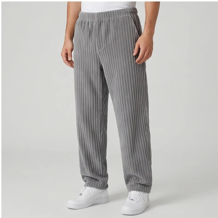 Man wearing baggy gray corduroy sweatpants with an elastic waistband, paired with white sneakers on a light background.
