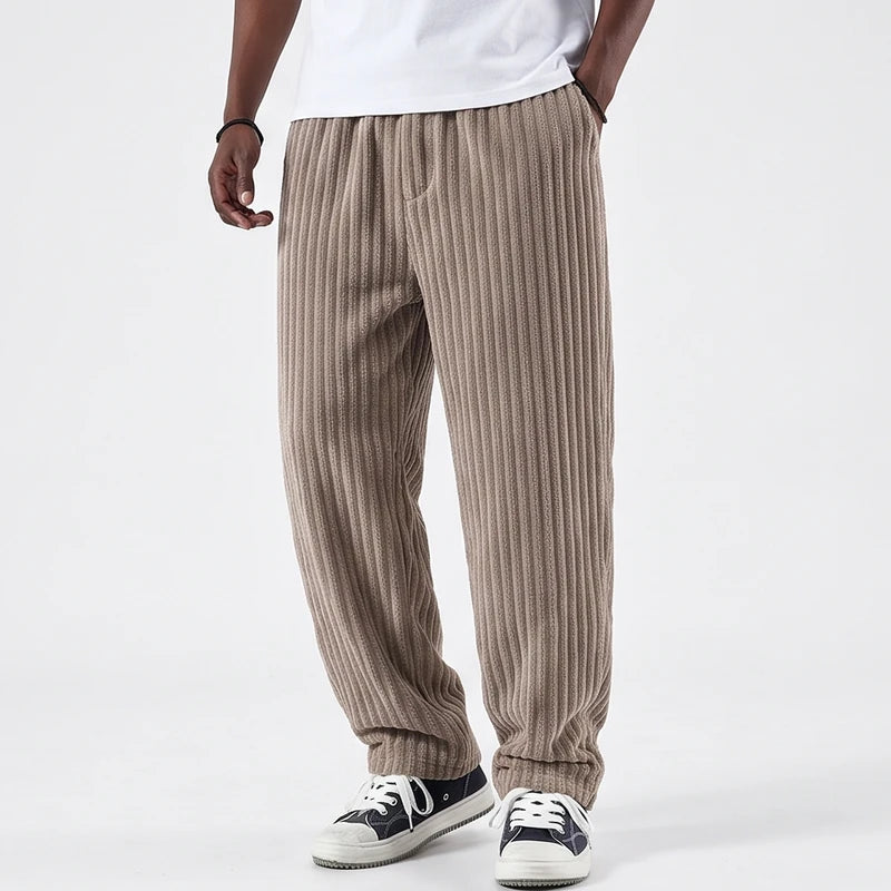 Man wearing beige corduroy pants with a relaxed, baggy fit, elastic waistband, and ribbed texture, standing on a white background.
