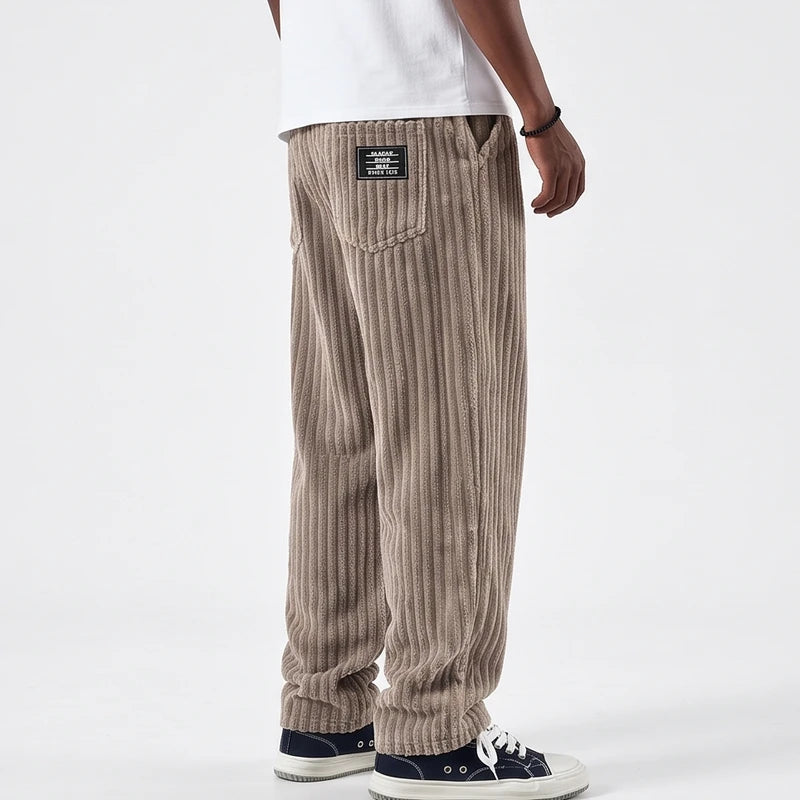 Man wearing baggy taupe corduroy pants with a black label on the back pocket, paired with dark sneakers.