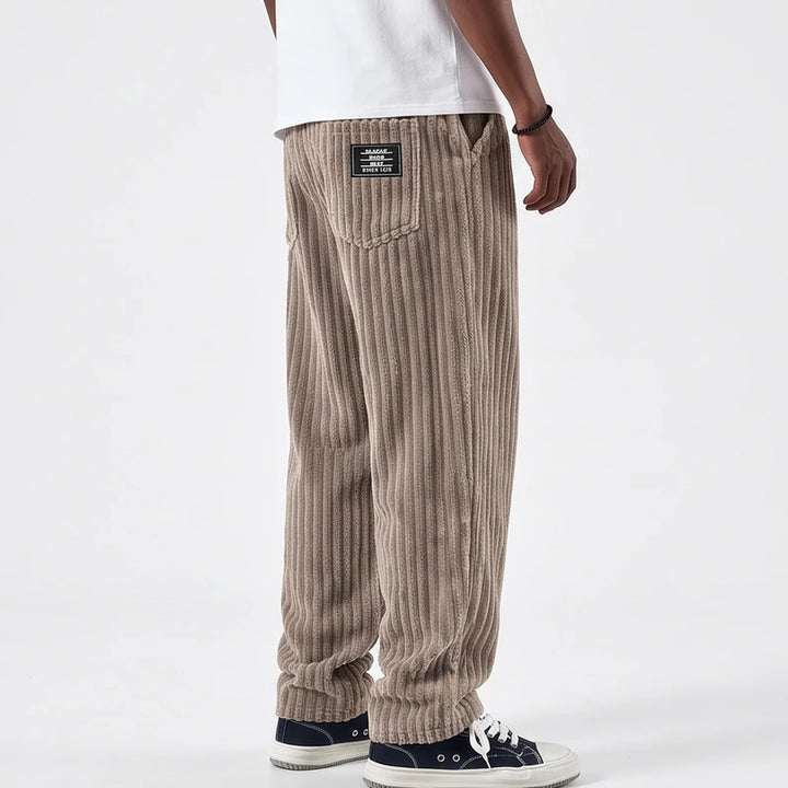 Man wearing baggy taupe corduroy pants with a black label on the back pocket, paired with dark sneakers.