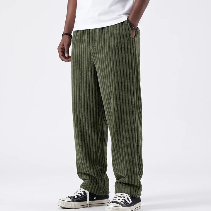 Man wearing olive green corduroy pants with a baggy fit, hands in pockets, paired with black canvas shoes.