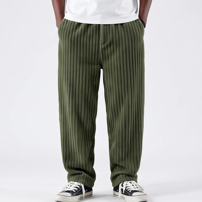 Man wearing baggy olive green corduroy pants with an elastic waistband and black sneakers on a white background.