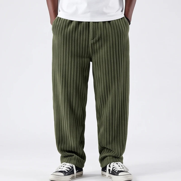 Man wearing baggy olive green corduroy pants with an elastic waistband and black sneakers on a white background.