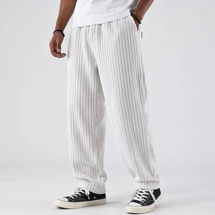 Man wearing white ribbed corduroy baggy pants with an elastic waist, paired with a white t-shirt and black sneakers.