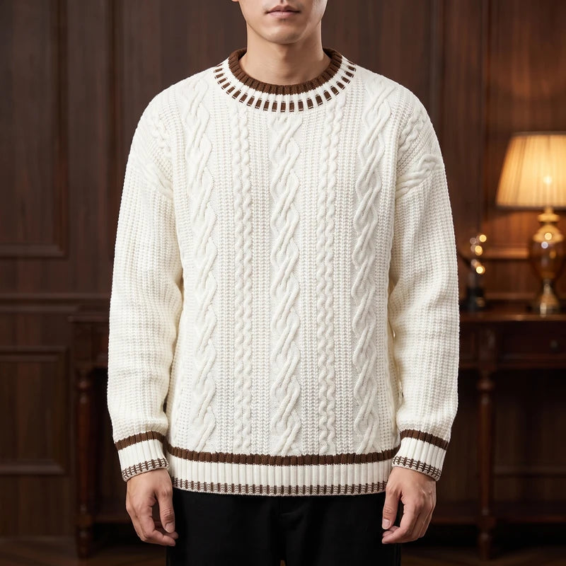 Man wearing an off-white cable-knit sweater with brown striped ribbed collar, cuffs, and hem in a wood-paneled room.