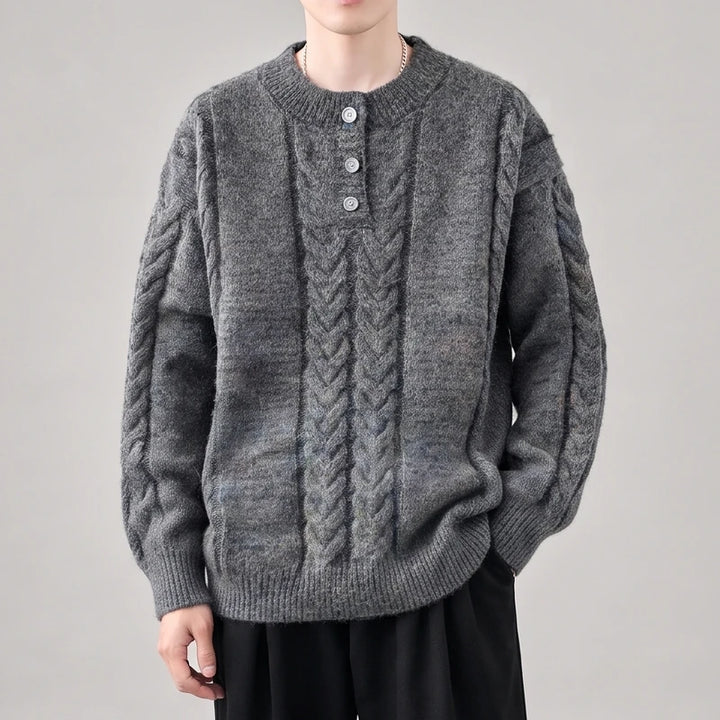 Man wearing a dark gray cable-knit sweater with a three-button henley placket and ribbed cuffs, against a light background.