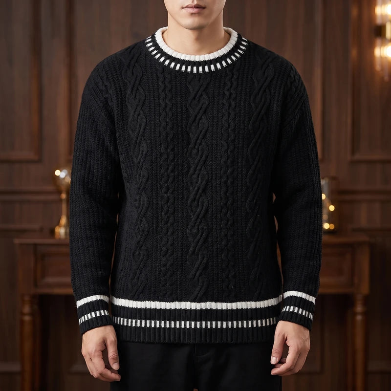 Man wearing a black cable-knit sweater with white striped ribbing at the neck, cuffs, and hem, standing indoors.