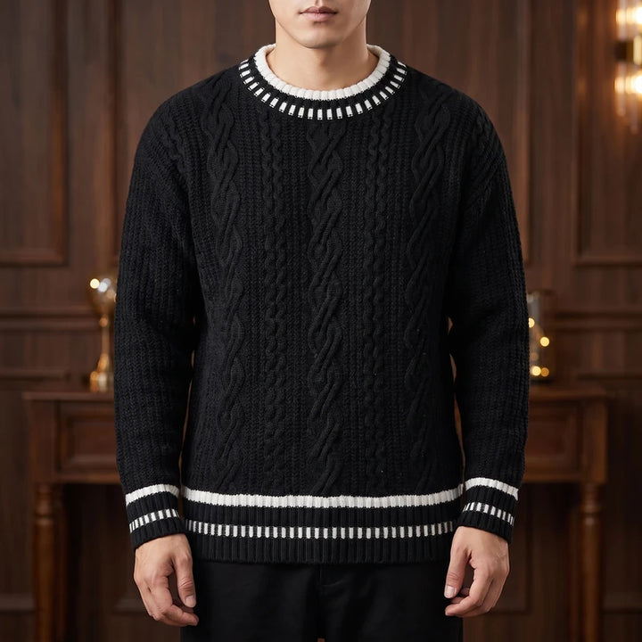 Man wearing a black cable-knit sweater with white striped ribbing at the neck, cuffs, and hem, standing indoors.