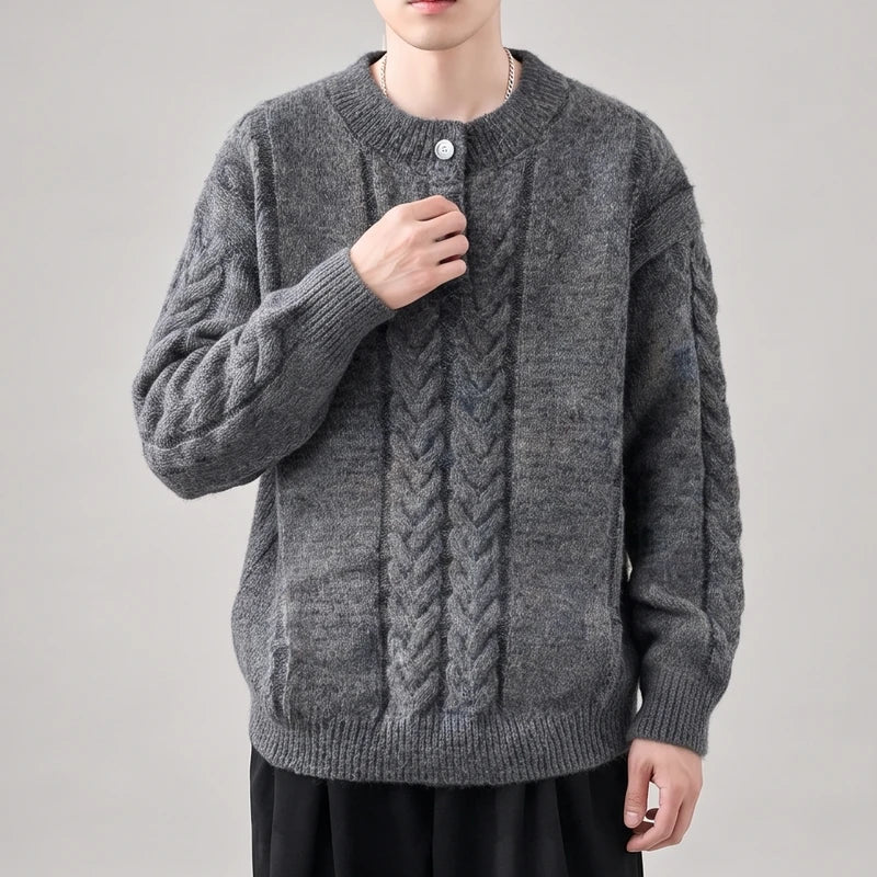 Man wearing a loose-fitting charcoal gray cable-knit sweater with a crew neck and a single white button at the collar.