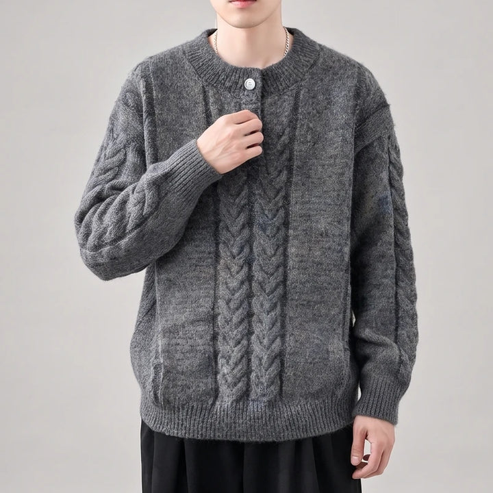 Man wearing a loose-fitting charcoal gray cable-knit sweater with a crew neck and a single white button at the collar.